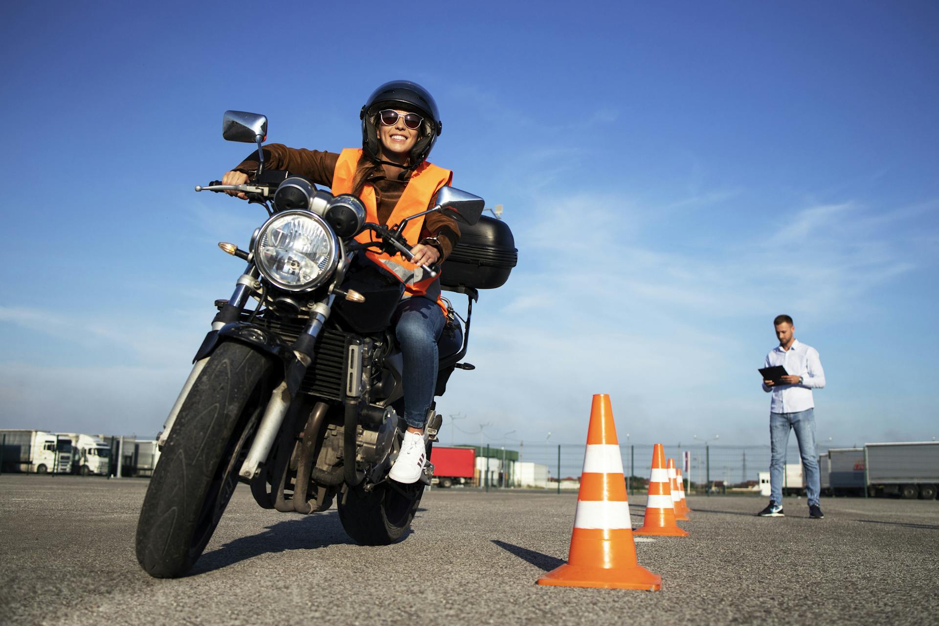 Persona con chaleco naranja y casco sobre motocicleta, persona al fondo.
