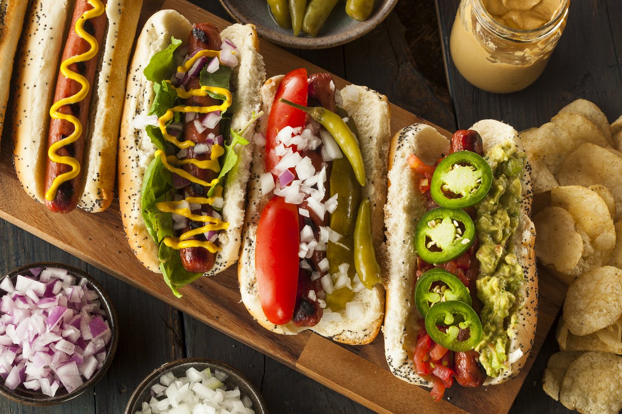 Hot dogs de diferentes estilos con aderezos y verduras
